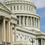Close-up of the U.S. Capitol building, featuring its architectural details and columns under a clear blue sky.
